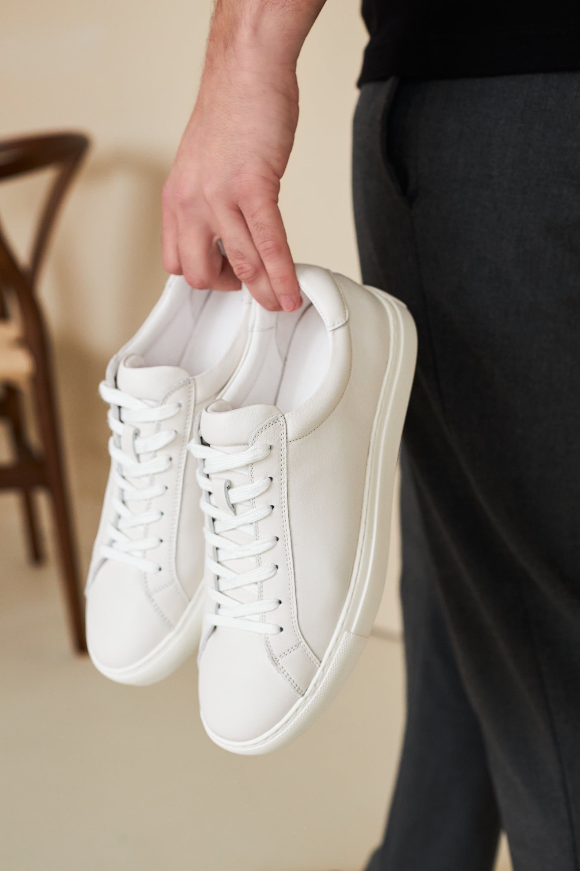 Hand holding a pair of white Neat sneakers, ready to trade in